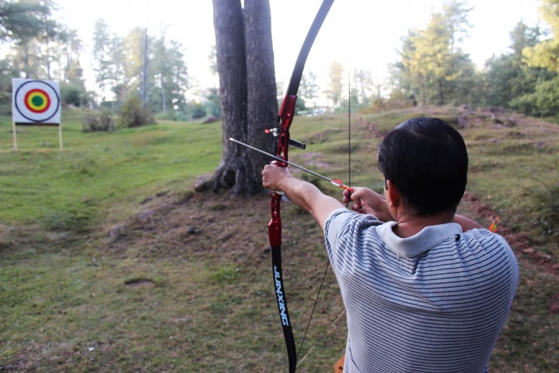 A visitor drawing a recurve bow at a target on the meadow