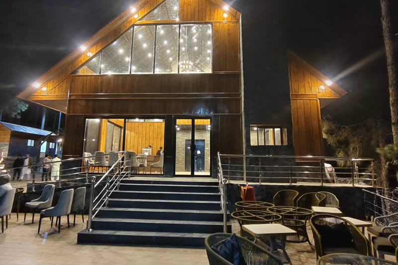 The resort's timber-and-glass restaurant lit up at night, with terrace seating