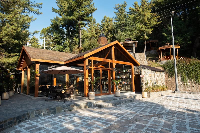Timber-and-glass clubhouse restaurant with a stone-paved courtyard among pines