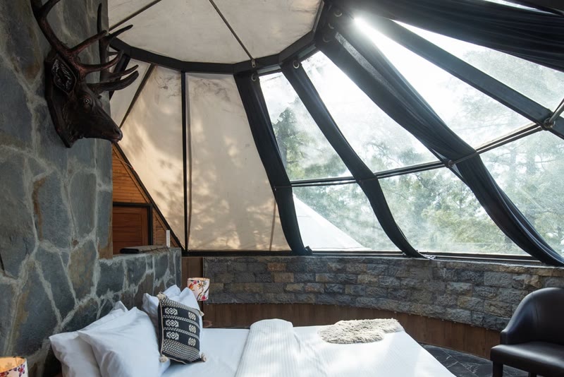 Inside an igloo unit: a bed beneath a glass-panelled roof and stone walls