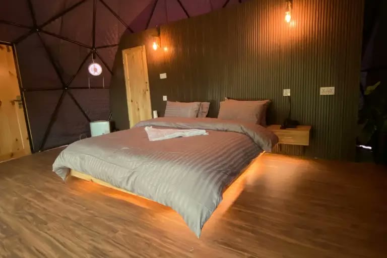 Inside a glamping dome: double bed, wooden floor and warm lighting