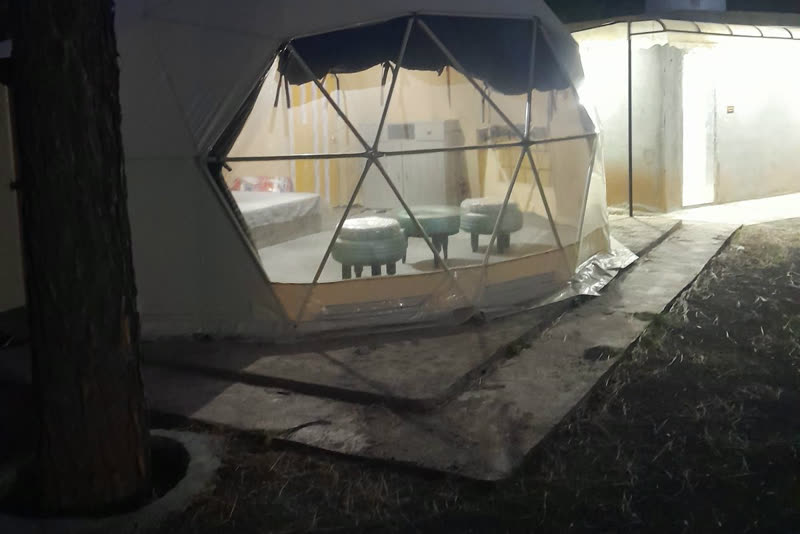 A glamping dome lit up at night, with beds and seating visible through its window