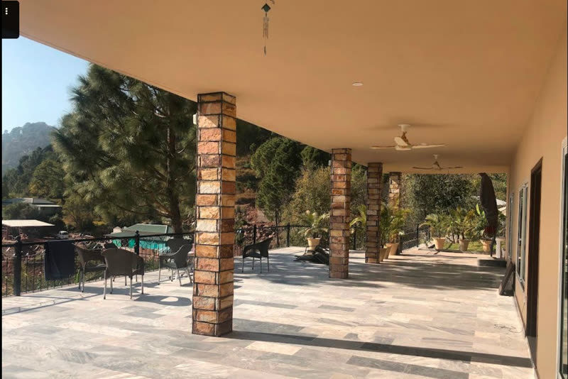 Covered stone terrace of the guest house with seating and views over the pines