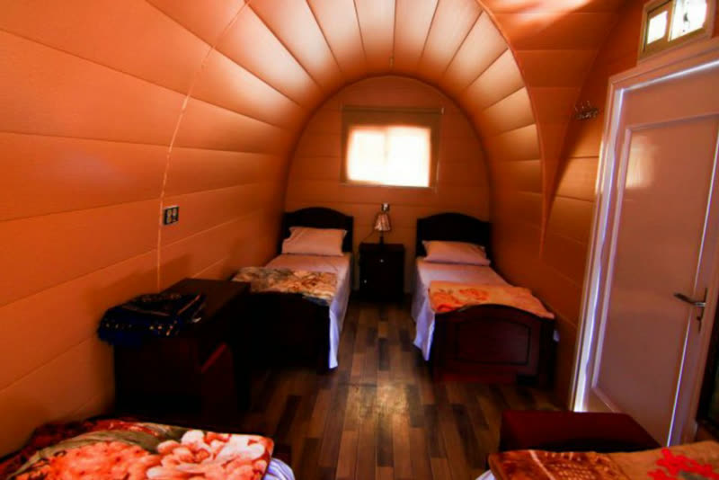 Inside a glamping pod: two single beds under a curved wooden ceiling