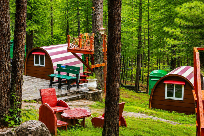 Barrel-shaped glamping pods with red-and-white striped roofs among tall pines at Patriata, with outdoor seating